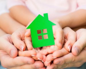 family-hands-holding-green-paper-house