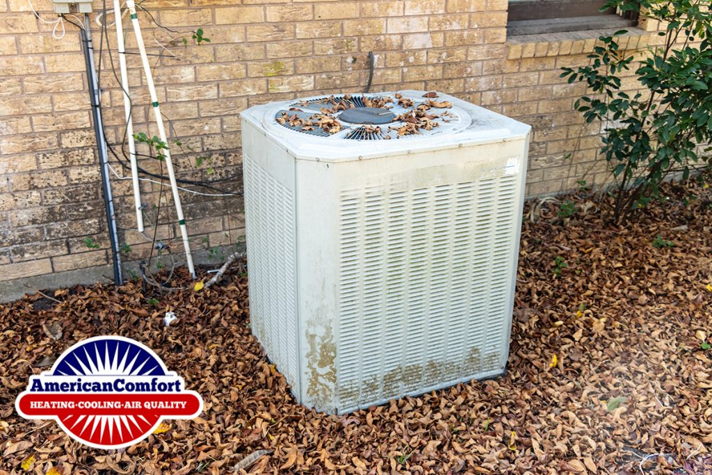An old air conditioning unit with dirt build up on the metal and autumn leaves scattered on top of and around it.